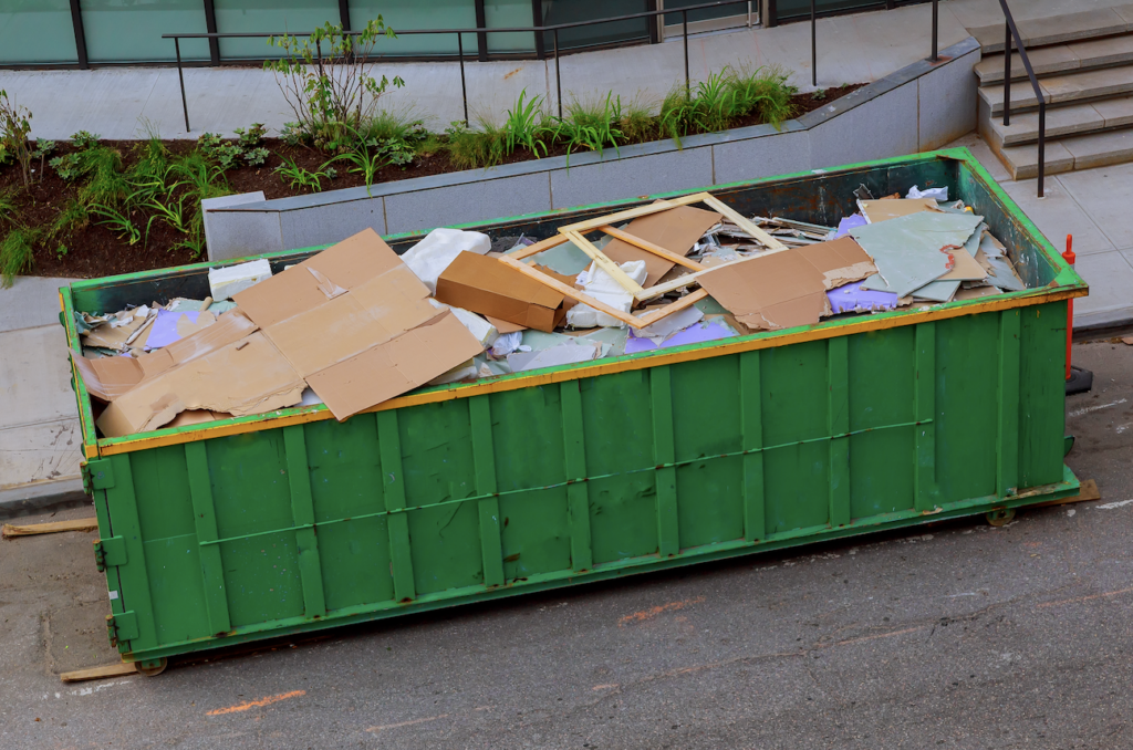 Feature image for an eco-friendly waste management blog, showcasing a vibrant, green dumpster full of debris. The background features a small business district in Jacksonville, Florida. This visually represents the blog's focus on innovative and effective waste management strategies for small businesses, highlighting the role of dumpster rental companies like Gopher Waste in fostering a greener future in and around Jacksonville, FL.