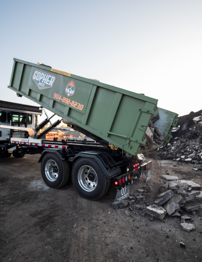 Roll-off truck unloading a green dumpster with construction debris onto a worksite in Jacksonville Beach